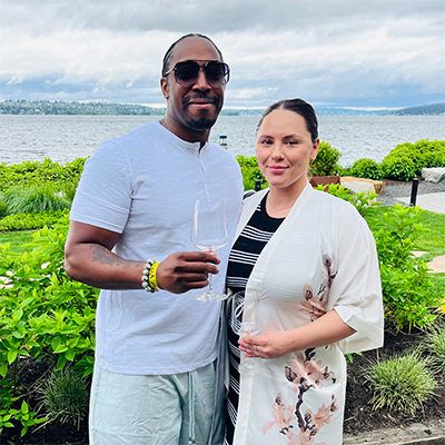 two people posing with wine glasses in front of water as the sunsets