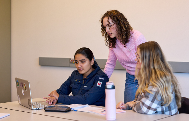 students looking at the laptop inside the classroom