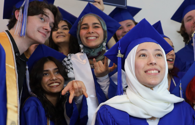 selfie of many students huddled together in graduation cap and gowns