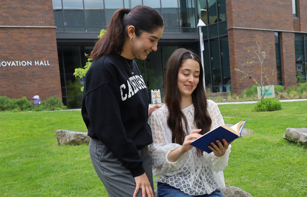 two students sitting on a rock outside of Innovation Hall reading a book