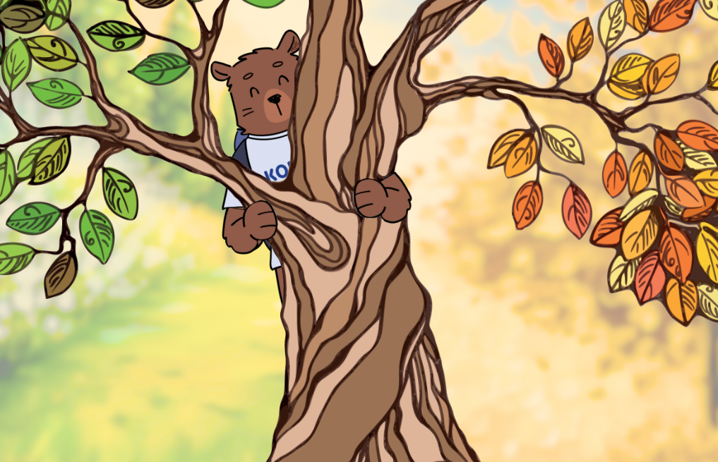 Kody bear behind a tree with green and orange leaves.