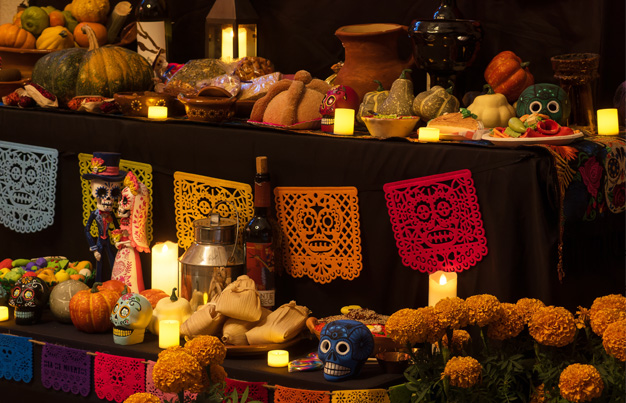 Día de los Muertos ofrenda with candles, sugar skulls, flowers, and gourds.