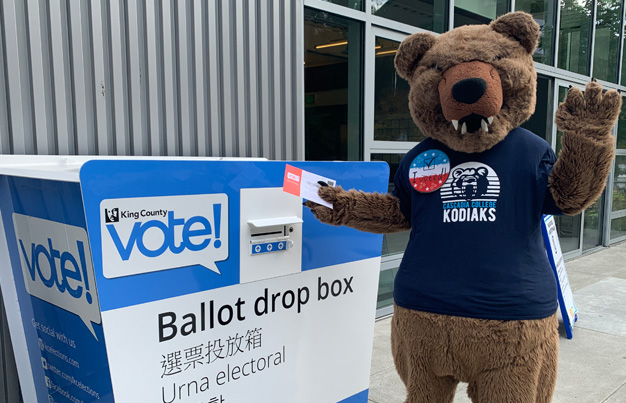 Kody bear mascot dropping ballot in voting box and waving
