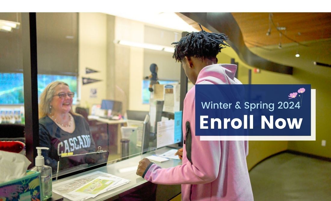 Student from the back wearing a pink hoodie talking through plexiglass to enrollment specialist wearing Cascadia long sleeve t-shirt and the text, 'Winder and Spring 2024; Enroll Now'