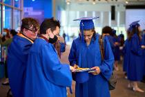Three graduates in blue gear looking at designed graduation caps