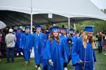 Cascadia College graduates in blue gowns and caps walking outside the tent at the ceremony