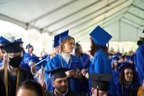 Two Cascadia College graduates in blue gowns and caps talking to each other under the tent at the graduation ceremony