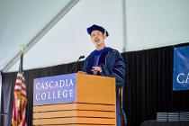 Cascadia College President Dr. Eric Murray in graduation garb speaking at podium