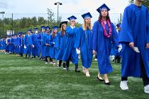 Cascadia College graduates in blue gowns and caps lining up on the field