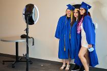 Three graduates in blue graduation gear in front of selfie ring