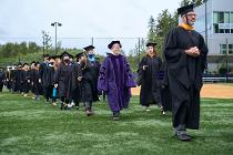 Cascadia College faculty and staff in black gowns and caps walking across the field