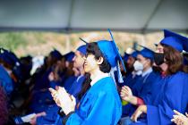 Graduates in blue gowns and caps sitting and clapping at the ceremony
