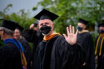 Faculty in black graduation gown and mask waving to the camera