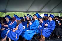 Graduates in blue gowns and caps sitting and clapping at the ceremony