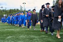 Cascadia College graduates in blue and black gowns and caps lining up on the field