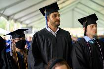 Three Cascadia College graduates in black gowns and caps standing up under the tent during the graduation ceremony