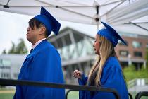 Two graduates in blue gowns and caps standing outside at the ceremony