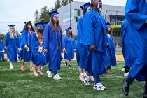 Cascadia College graduates in blue gowns and caps lining up on the field