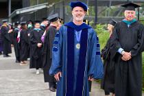 Cascadia College President, in a blue graduation gown, smiling at the camera with a member of the college board of trustee
