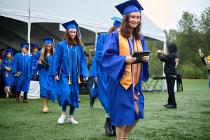 Cascadia College graduates in blue gowns and caps rushing out after collecting their diploma in the rain