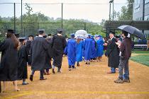 Graduates walking out in the rain as people cheer from the sides